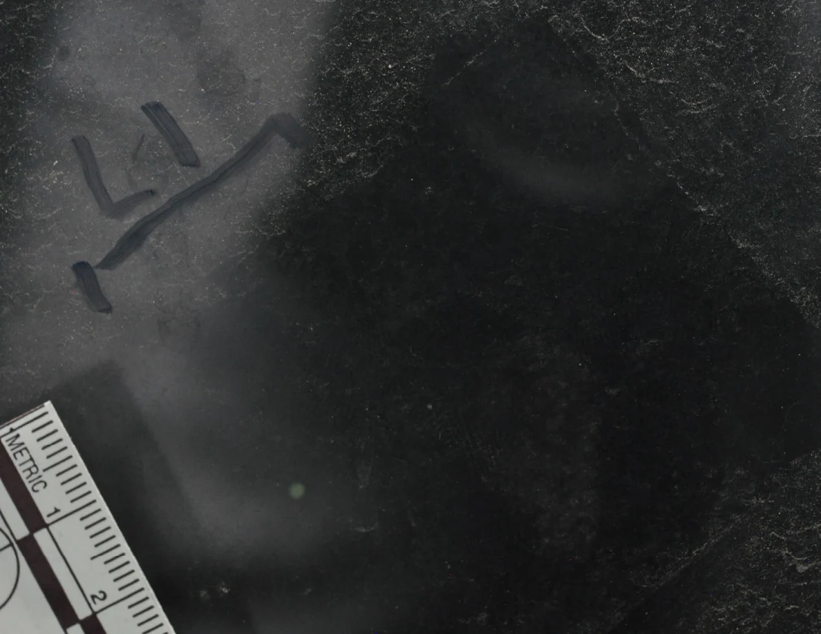 Dark glass close-up with reflected light, an arrow-shaped marker and a metric scale.
