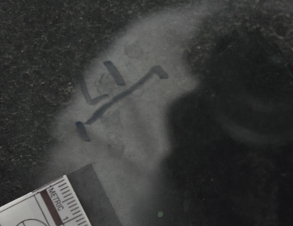 Dark glass close-up with reflected light, an arrow-shaped marker and a metric scale.