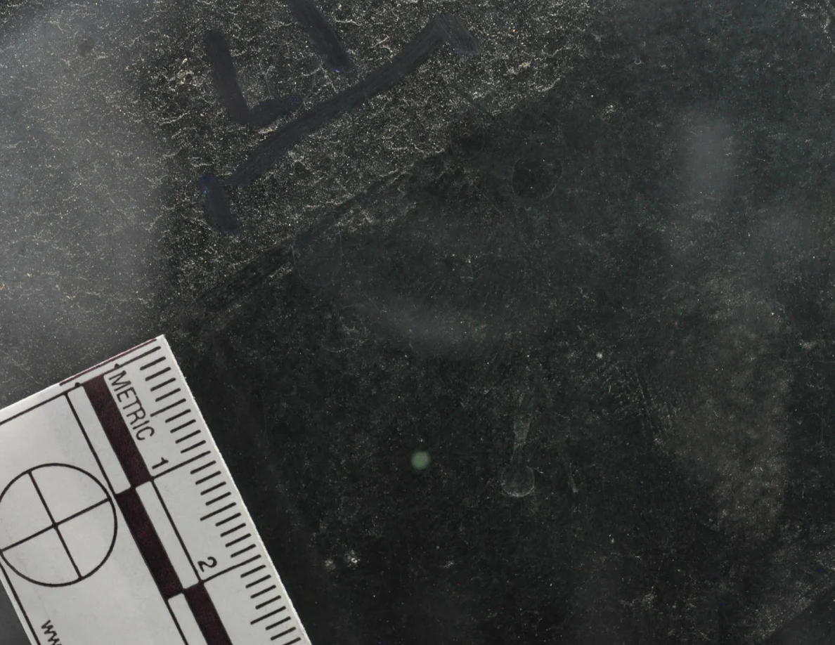 Dark glass close-up with reflected light, an arrow-shaped marker and a metric scale.