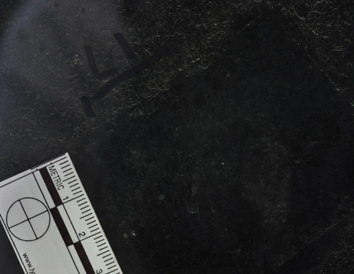 Dark glass close-up with reflected light, an arrow-shaped marker and a metric scale.