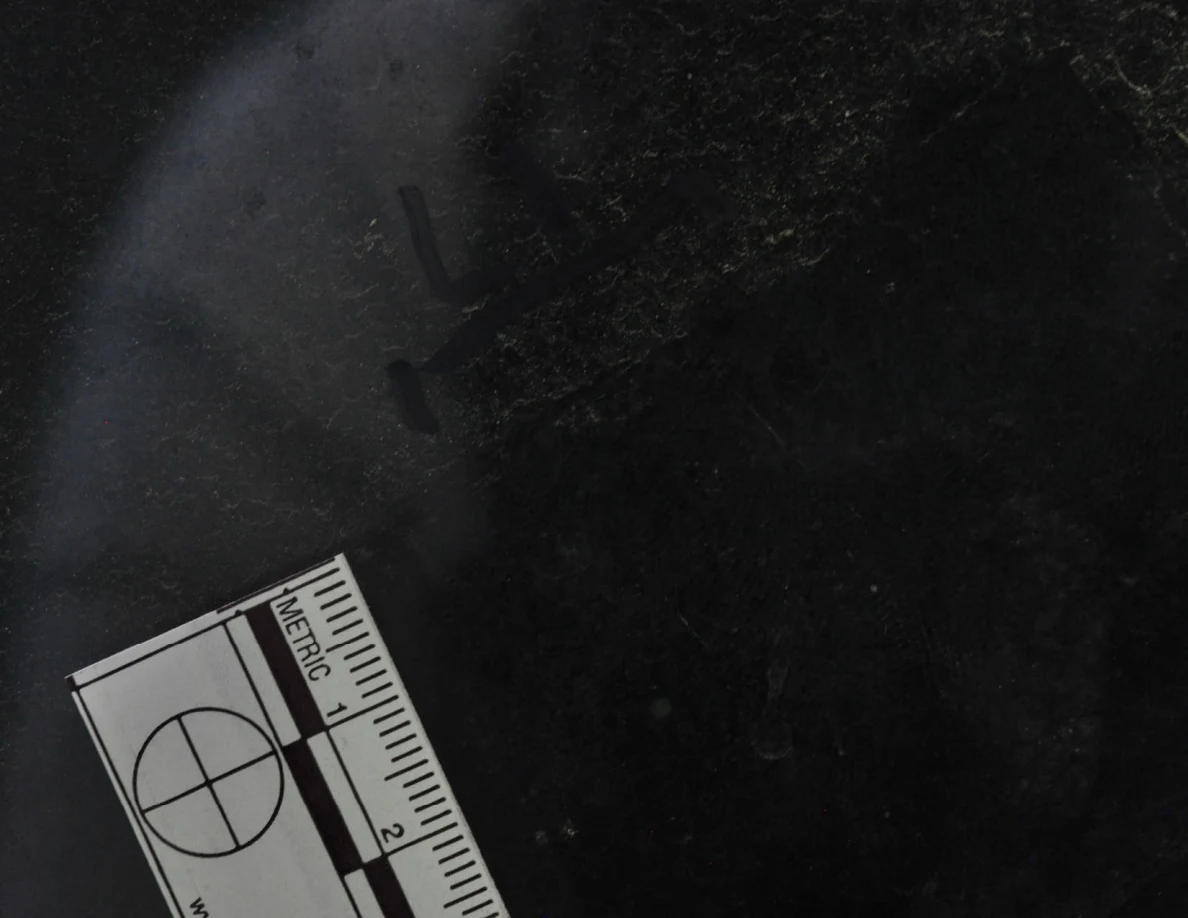 Dark glass close-up with reflected light, an arrow-shaped marker and a metric scale.