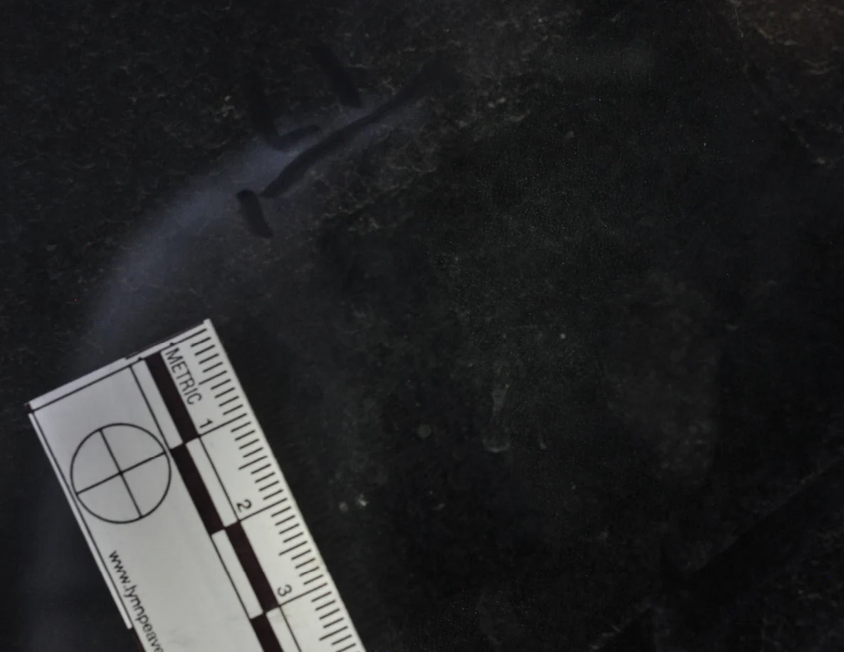 Dark glass close-up with reflected light, an arrow-shaped marker and a metric scale.