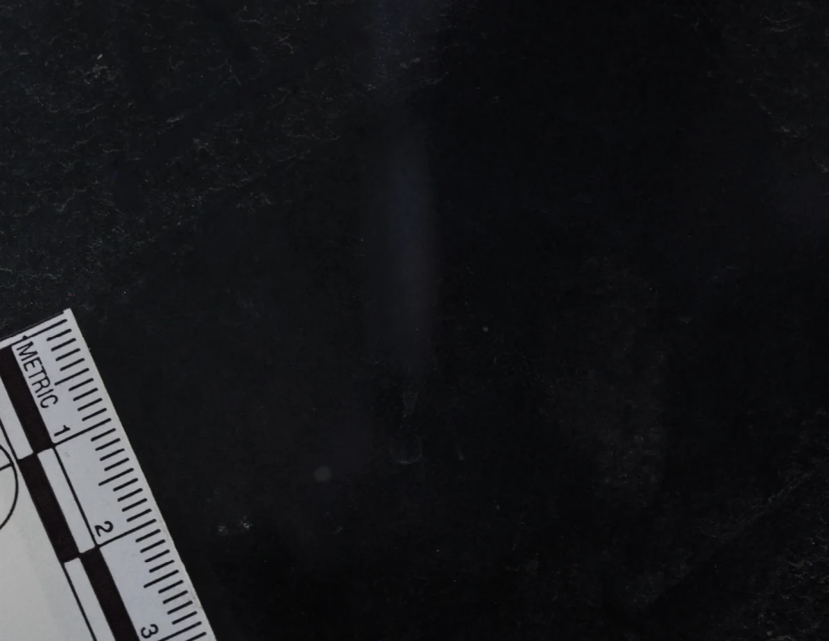 Dark glass close-up with reflected light, an arrow-shaped marker and a metric scale.