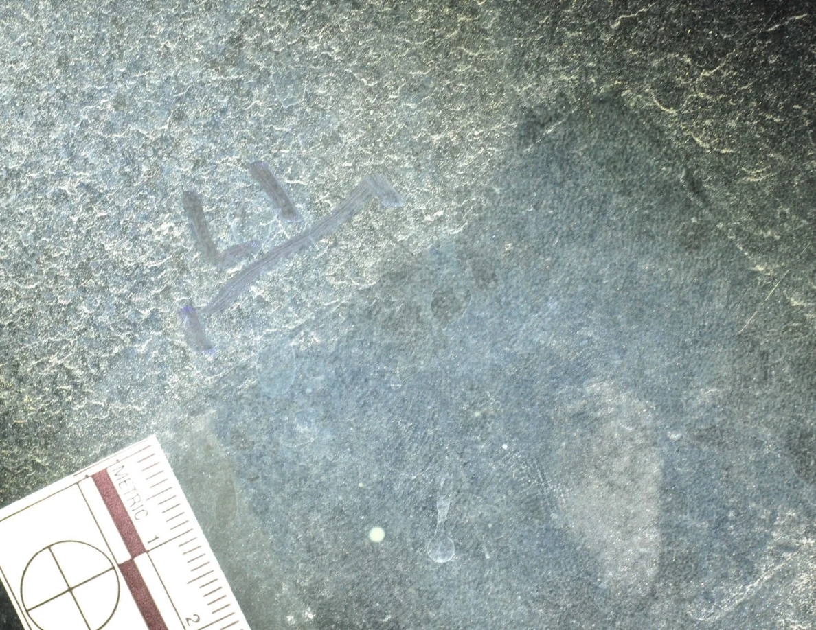 Illuminated close-up of glass with an arrow-shaped marker, a small pale dot and a metric scale.