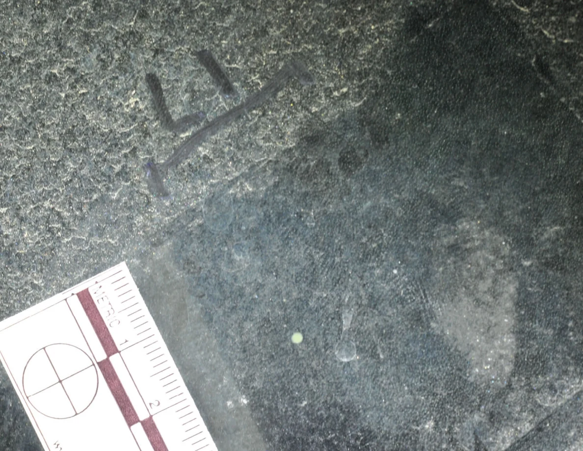 Illuminated close-up of glass with an arrow-shaped marker, a small pale dot and a metric scale.