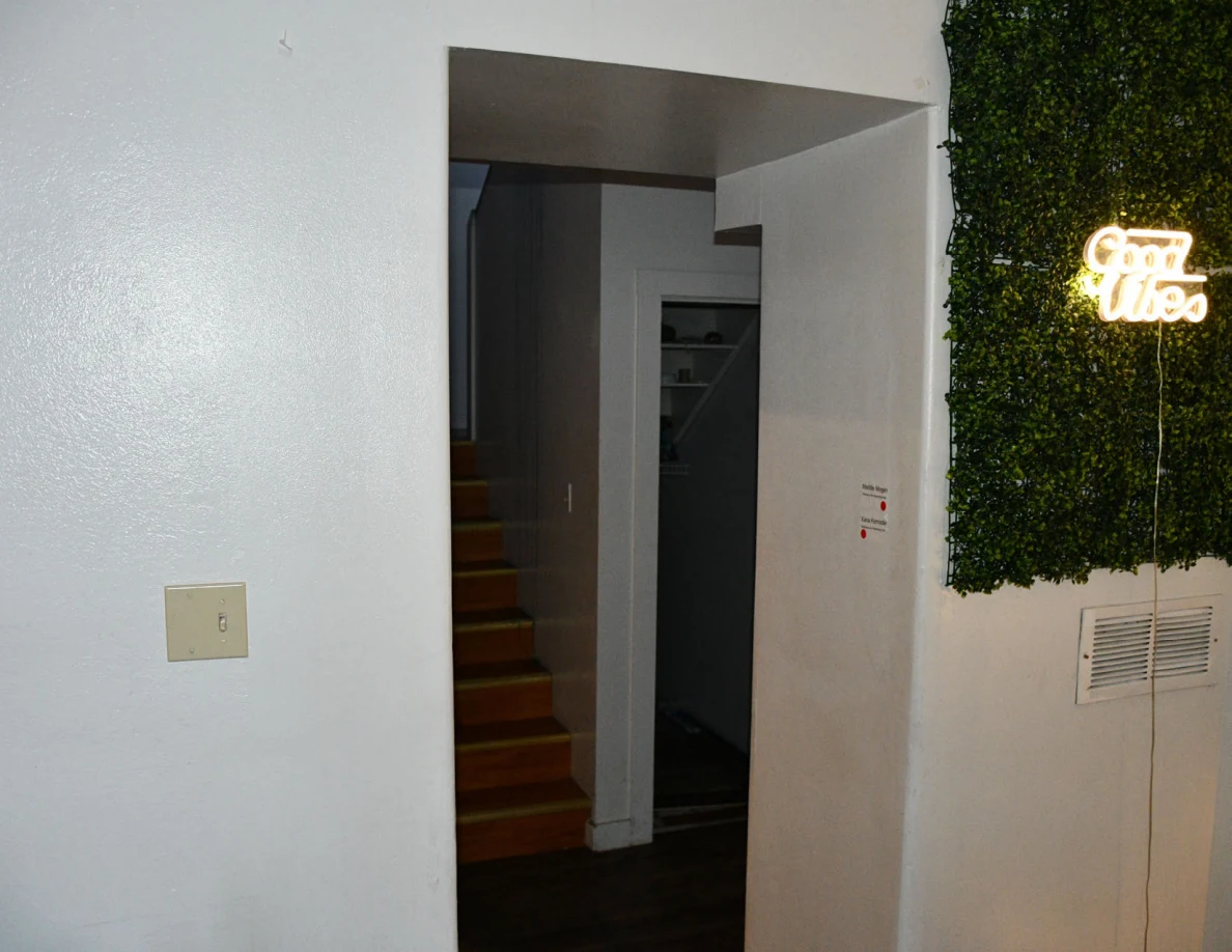 Interior doorway beside a green decorative wall panel and illuminated Good Vibes sign; wooden stairs are visible beyond.