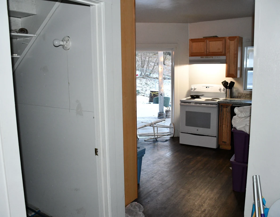 View through an interior doorway toward a kitchen with a stove, wood cabinets and an open exterior door.