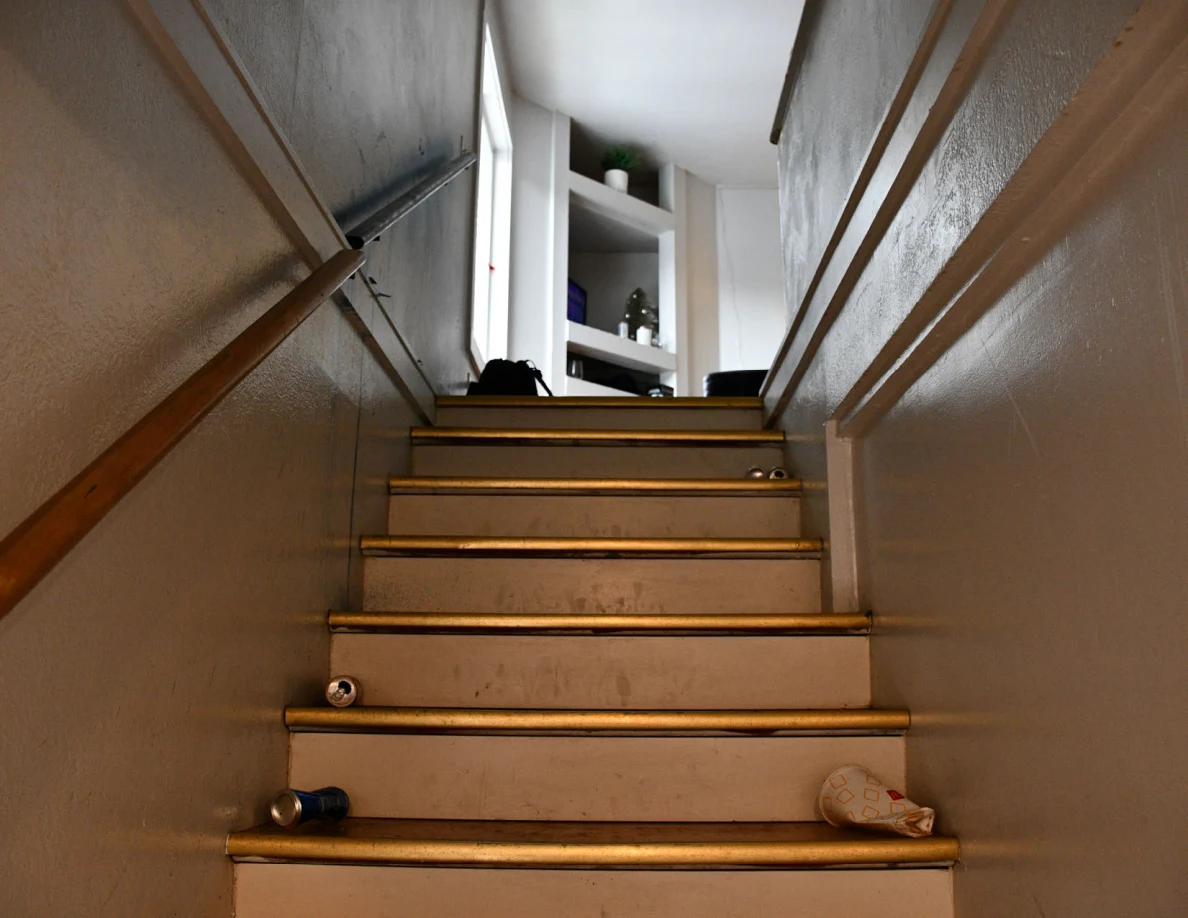 Wooden staircase with handrails, drink containers on the steps and shelving at the top.