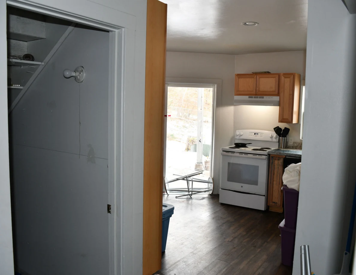 Doorway view into a kitchen with a white stove, wooden cabinets and an open exterior door.
