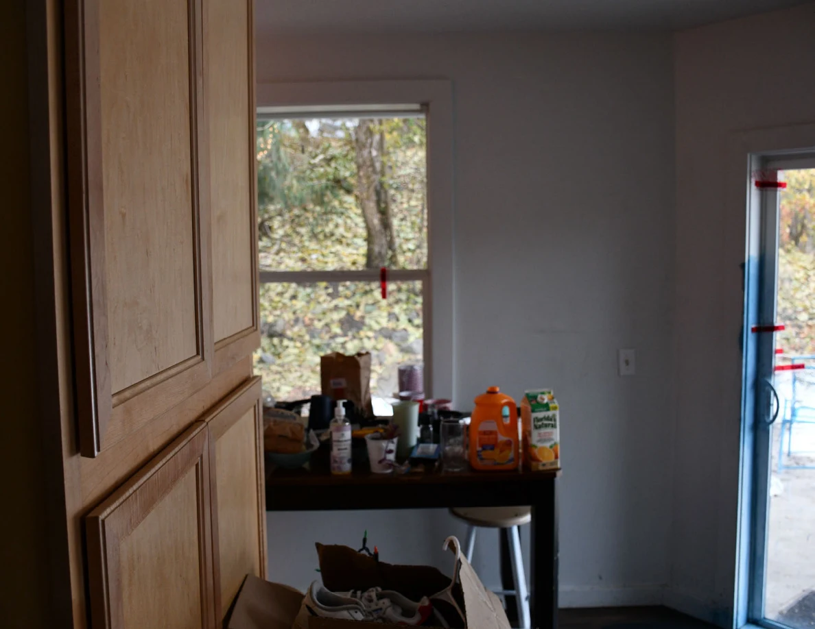 View past a wooden cabinet toward a kitchen table covered with drinks and a sliding glass door.