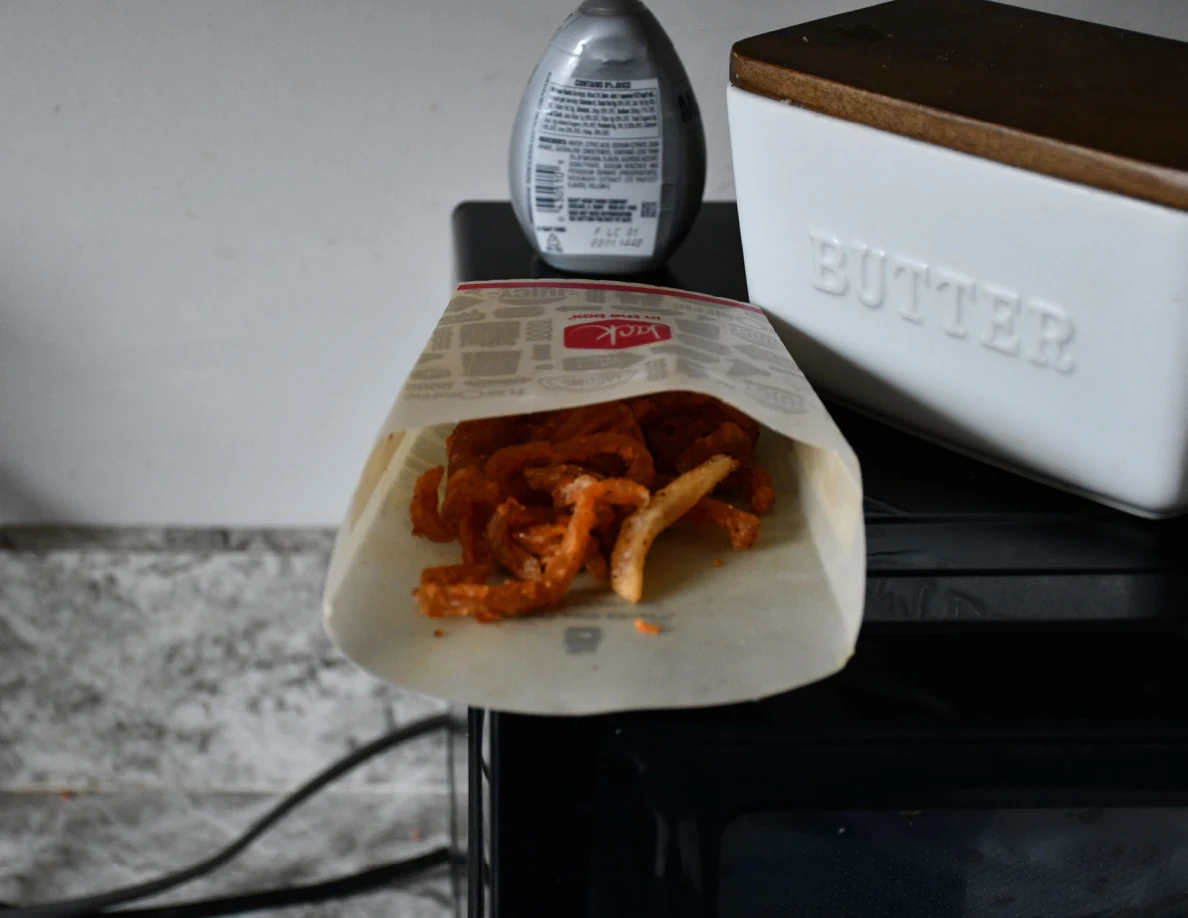 Close view of fries in a paper carton on top of a microwave beside a butter container.