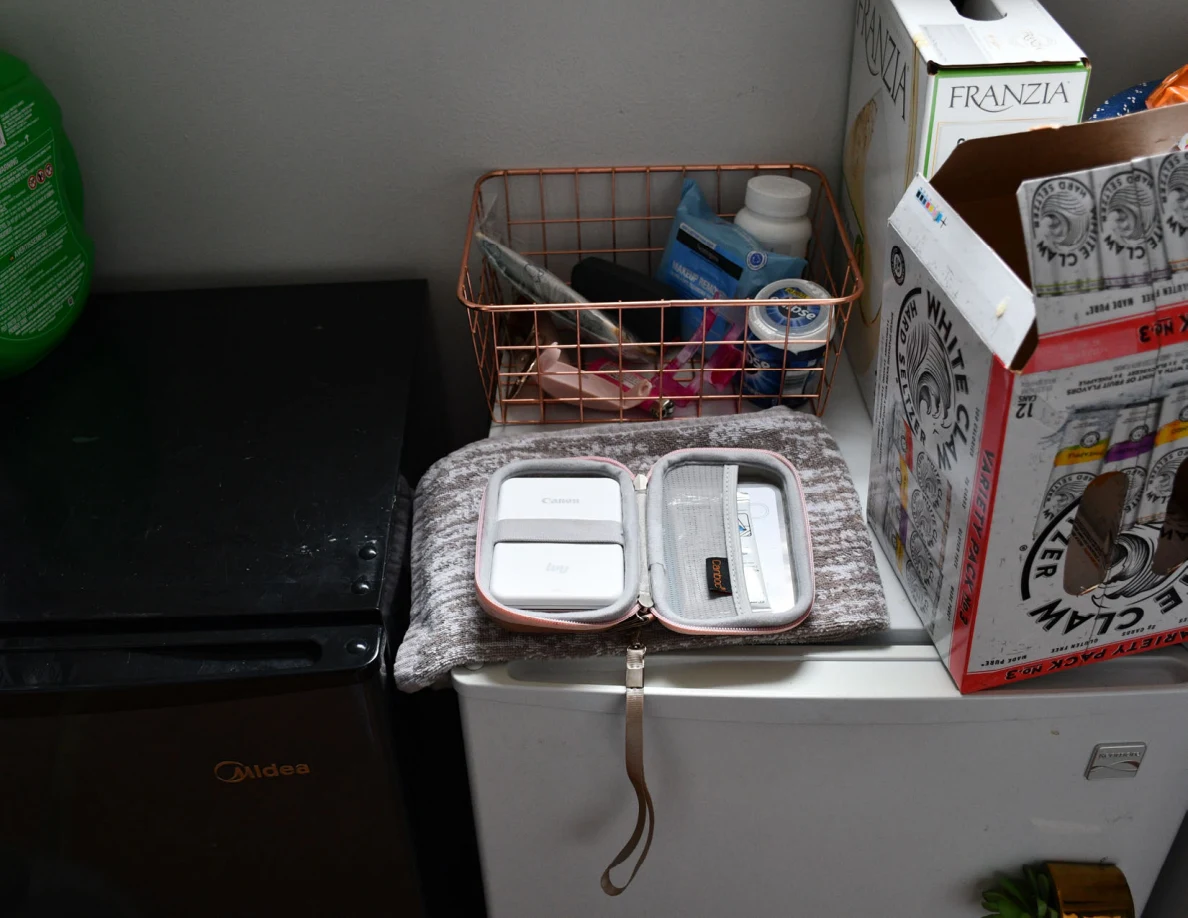 Open pink zippered case containing small white rectangular items on a folded cloth beside a wire basket.