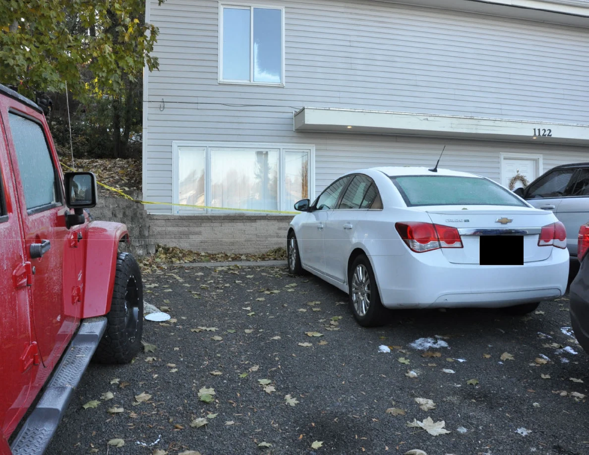 White sedan parked beside a red Jeep in front of a gray-sided house; license plate redacted.