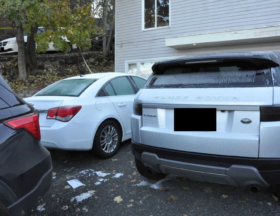 Rear views of a white sedan and silver Range Rover parked beside a gray-sided house.