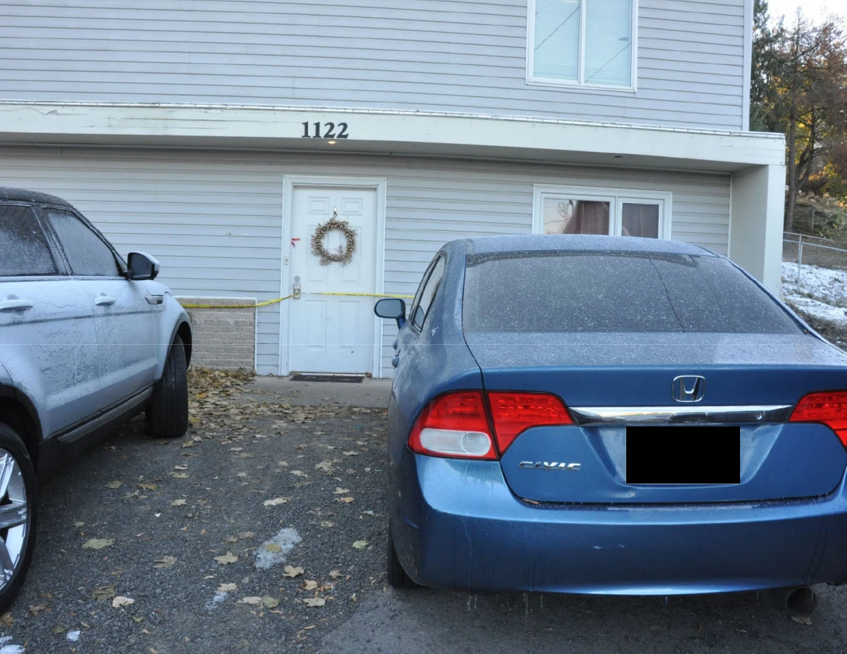 Blue Honda Civic parked by the front door of a house numbered 1122, with yellow tape across the entrance.
