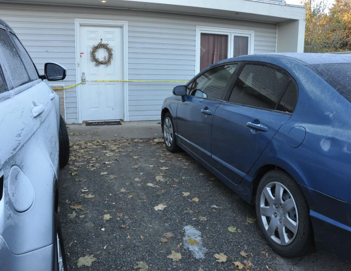 Blue sedan parked beside a white front door with a wreath and yellow tape.