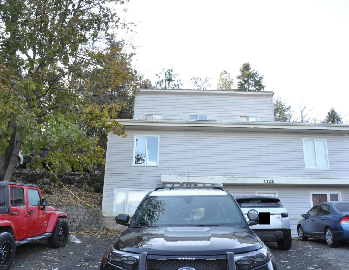 Gray-sided multistory house with a police SUV and several other parked vehicles in front.