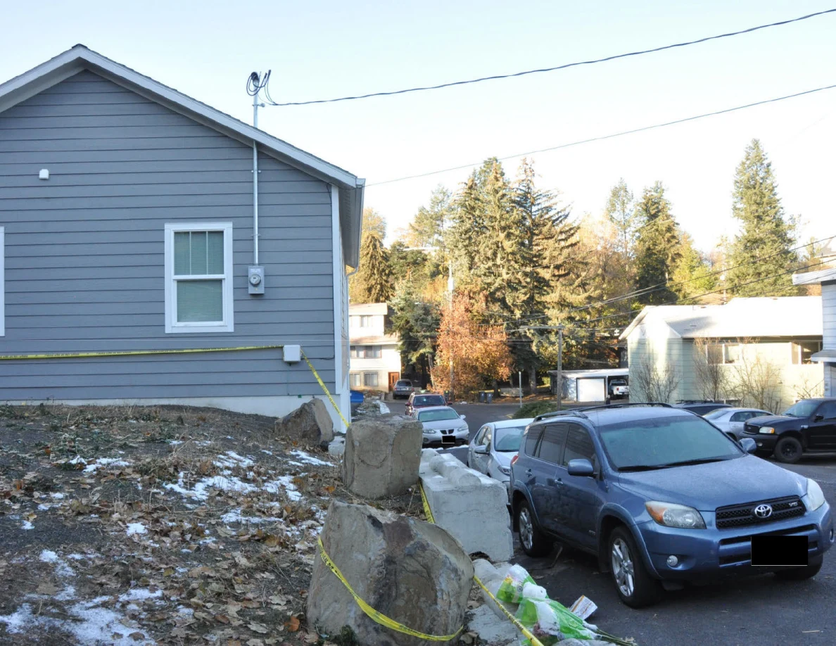 Blue SUV parked beside a gray house and stone retaining wall, with yellow tape along the slope.