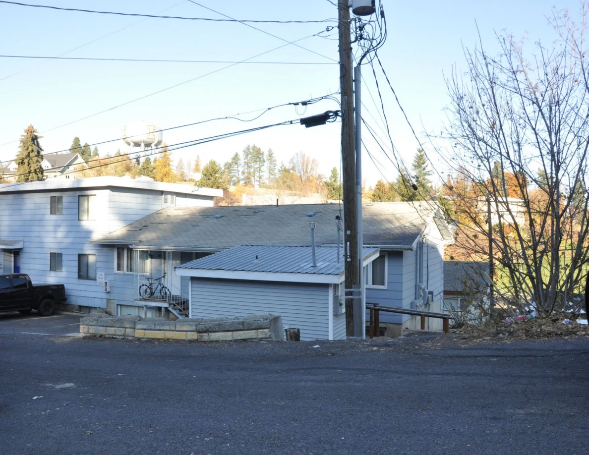 View across asphalt toward light-colored residential buildings and a wooden utility pole.