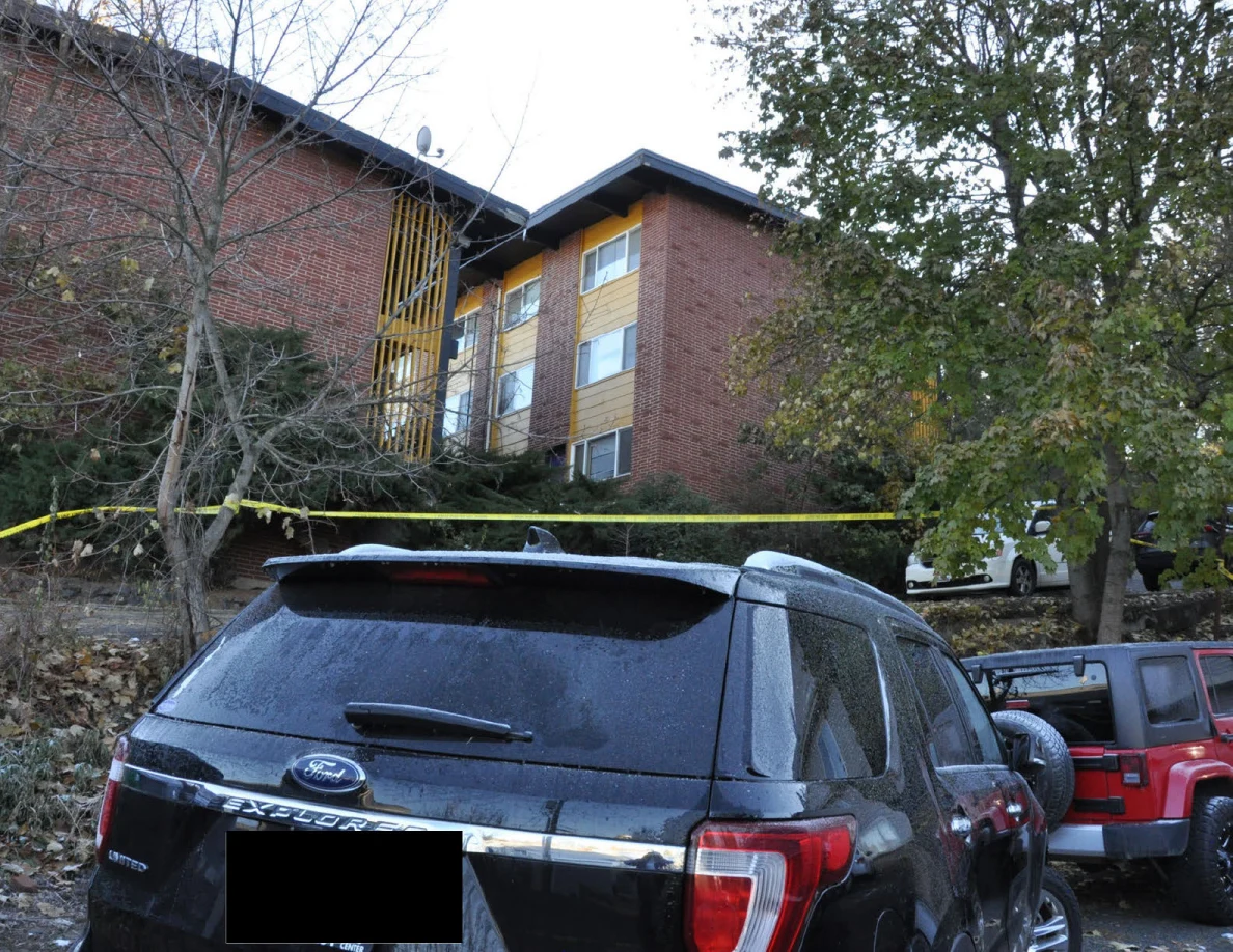 Black Ford SUV and red Jeep below a multistory brick building, with yellow tape across the slope.