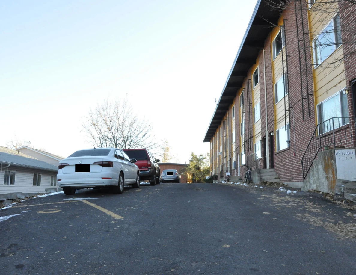 Sloping parking area beside a brick apartment building with parked cars and yellow space markings.