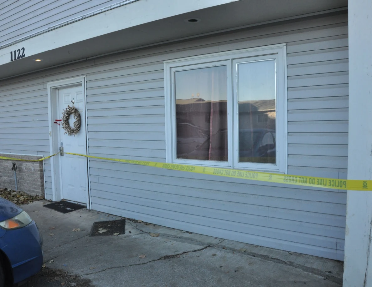 White front door and window crossed by yellow police tape on a gray-sided house.
