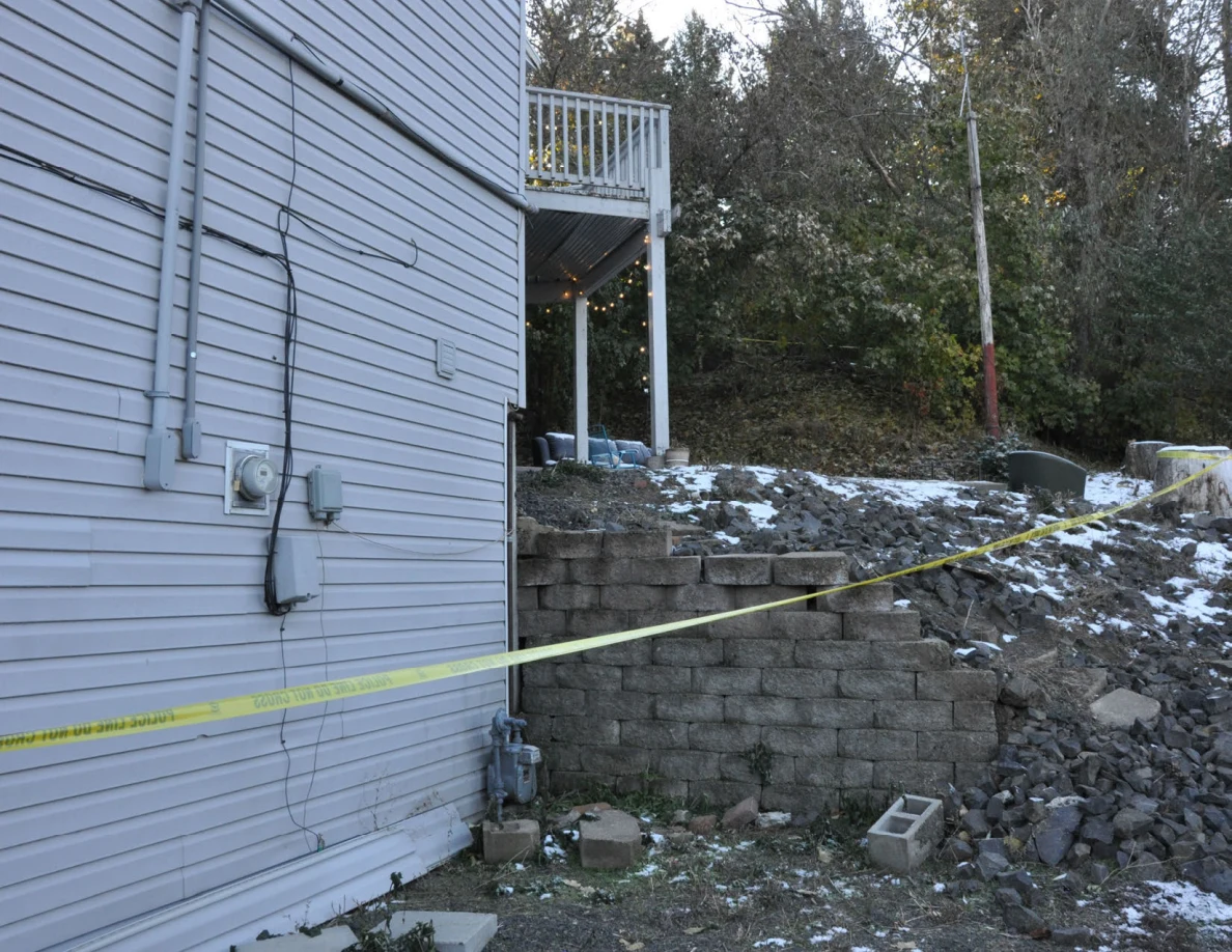 House electrical meter beside a block retaining wall, snow patches and yellow tape.