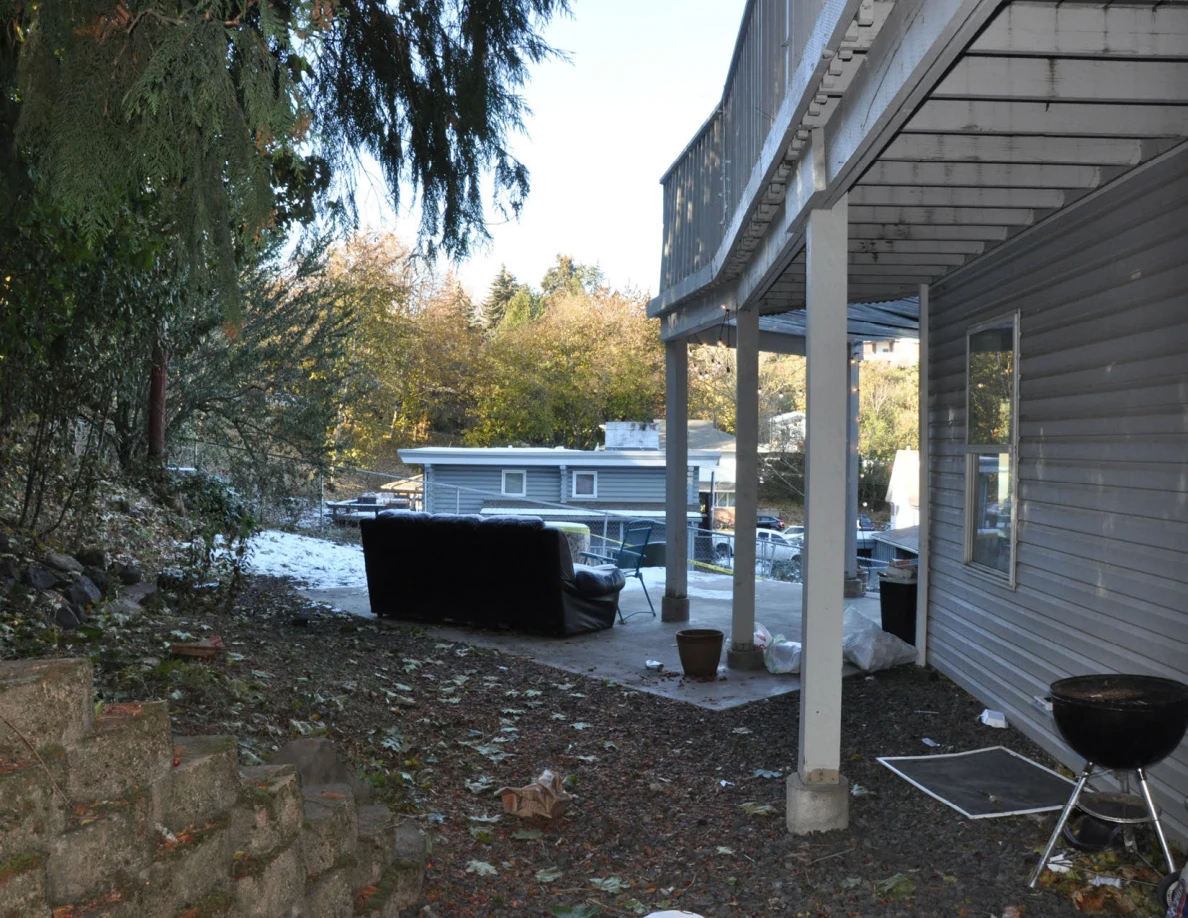 Rear patio beneath a raised deck with a sofa, grill, window and support posts.