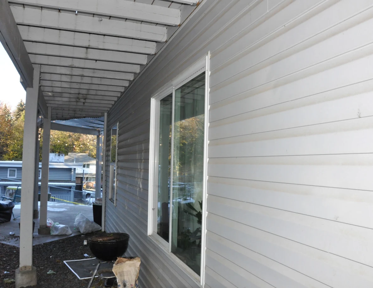 House window and gray siding beneath a raised deck, with a kettle grill below.