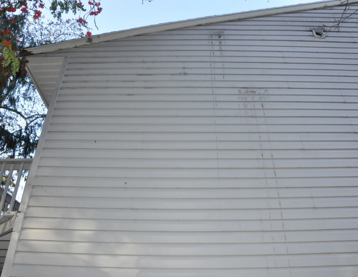 Upward view of gray exterior siding with vertical streaks below the roofline.