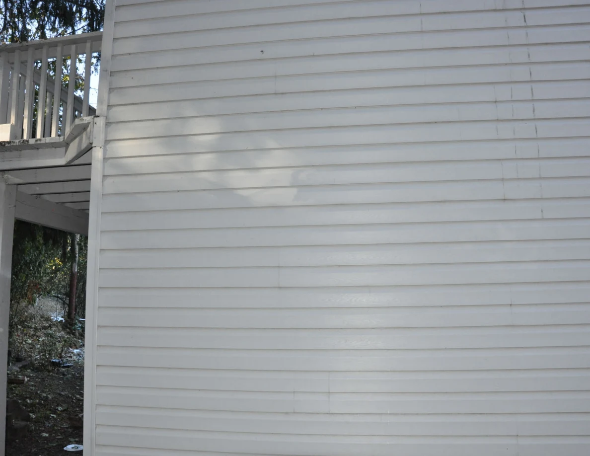 Gray exterior siding with tree shadows and a deck edge at left.