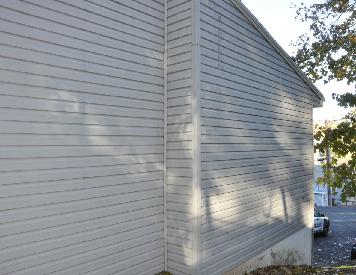 Gray house siding and projecting corner with shadows from nearby trees.