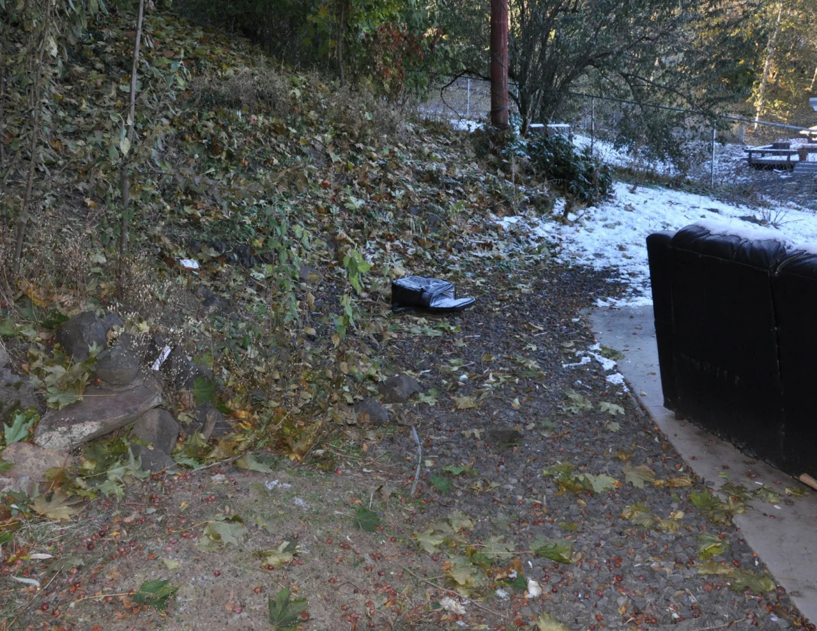 Snow and leaves beside an outdoor sofa, with a dark bag near the slope.