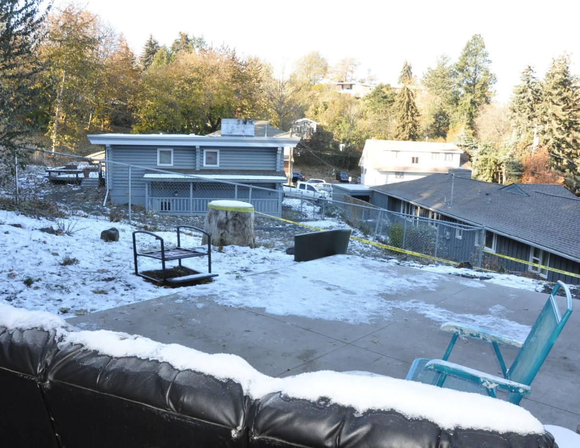 Snowy backyard overlooking neighboring houses, with a sofa, turquoise chair and overturned metal furniture.