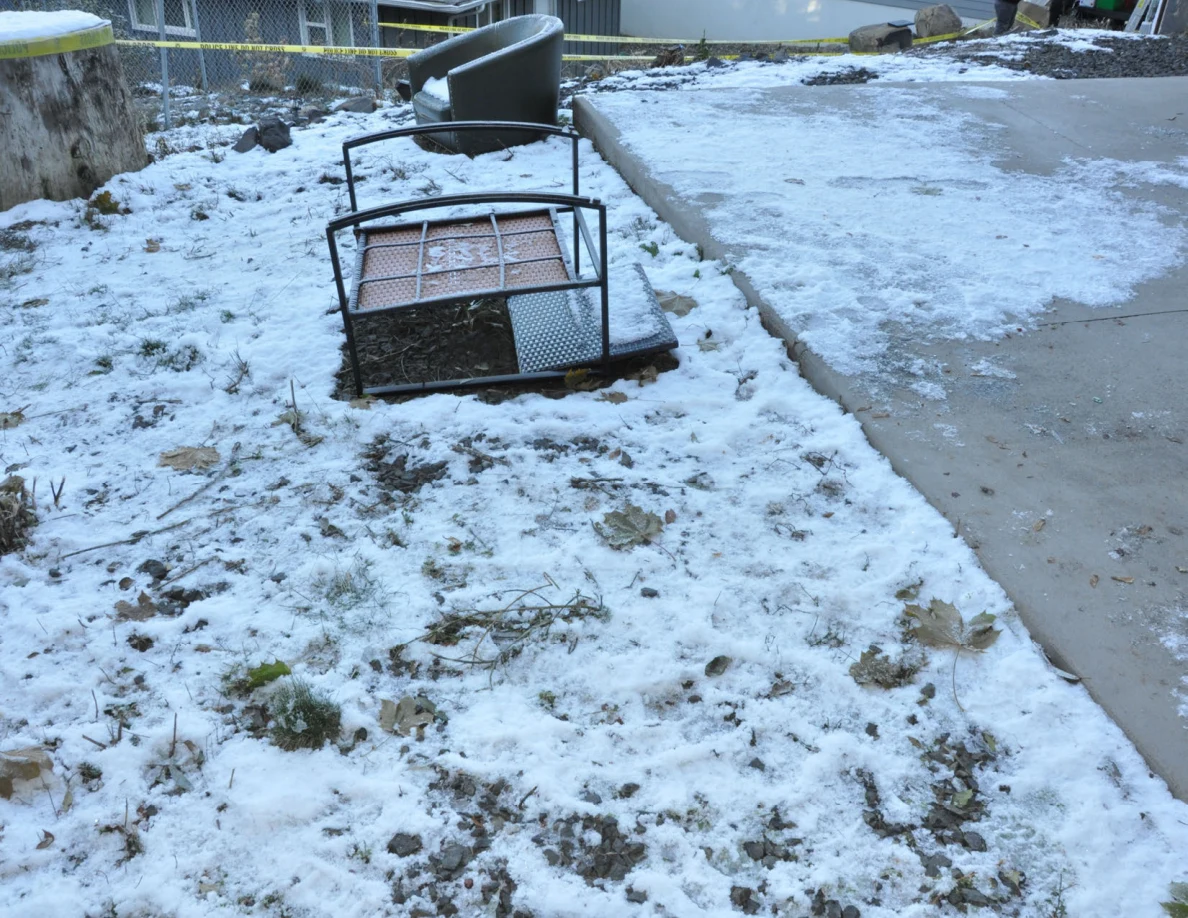 Overturned metal patio furniture on snowy ground beside a concrete slab and green chair.