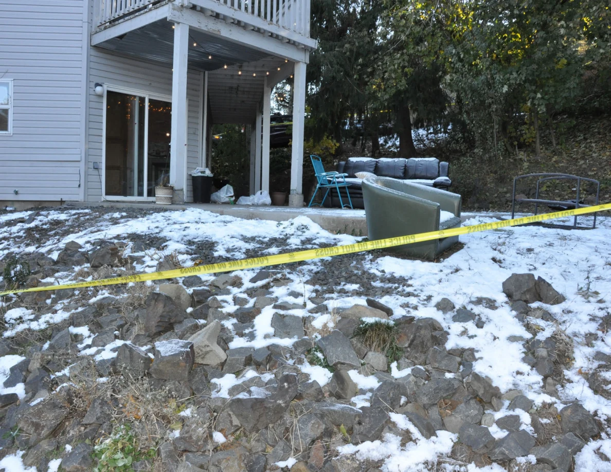 Snow-covered rocky slope crossed by yellow tape in front of a patio with chairs and sofa.
