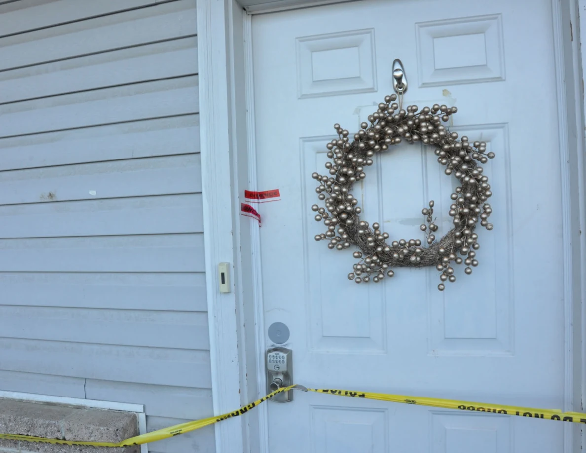 Close view of white front door, decorative wreath, keypad lock and yellow tape.