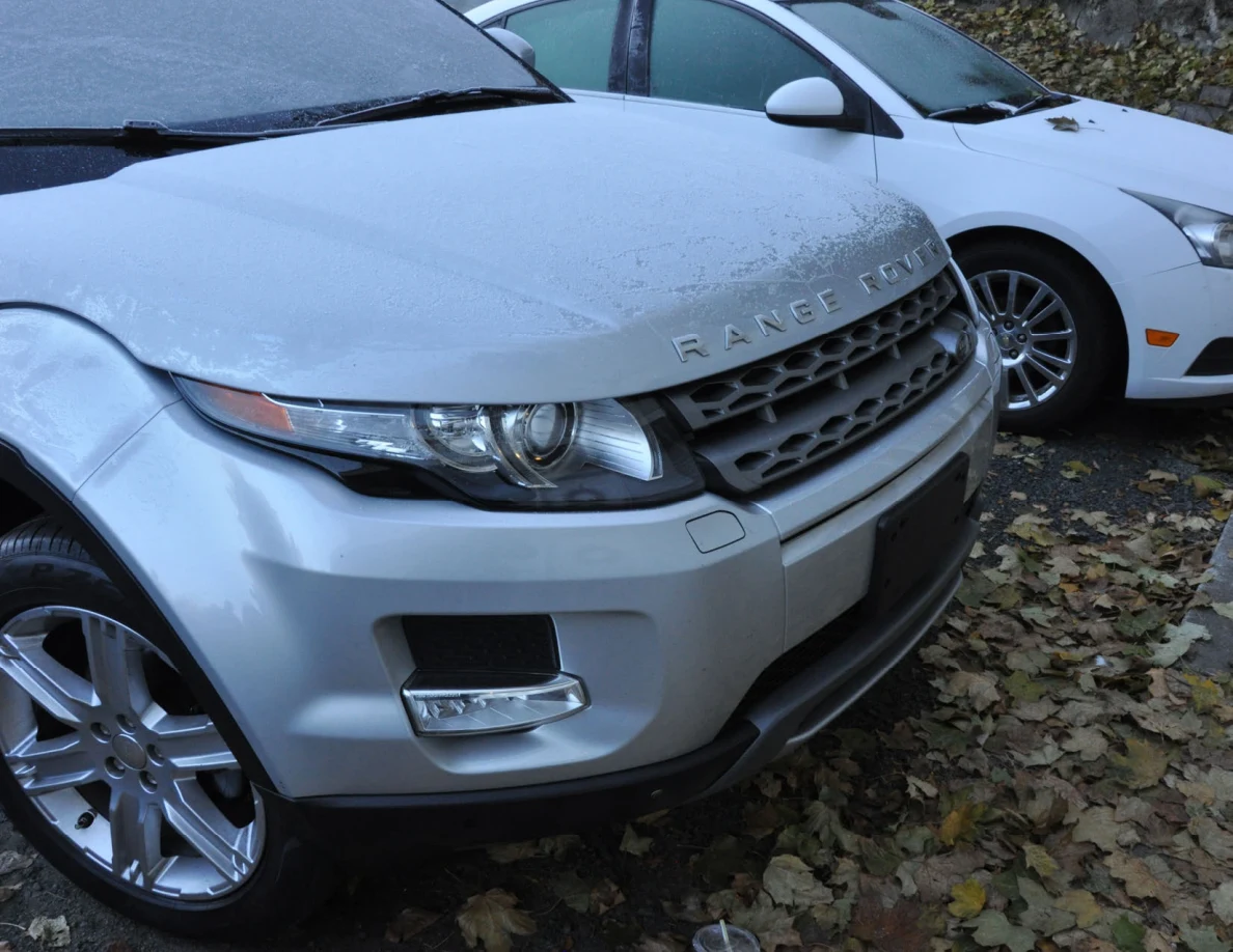 Front of a silver Range Rover beside a white sedan, with moisture on the hood.