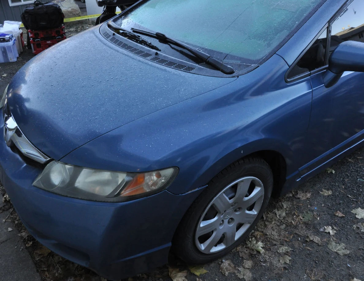 Front quarter of a blue sedan with moisture on the hood and windshield.