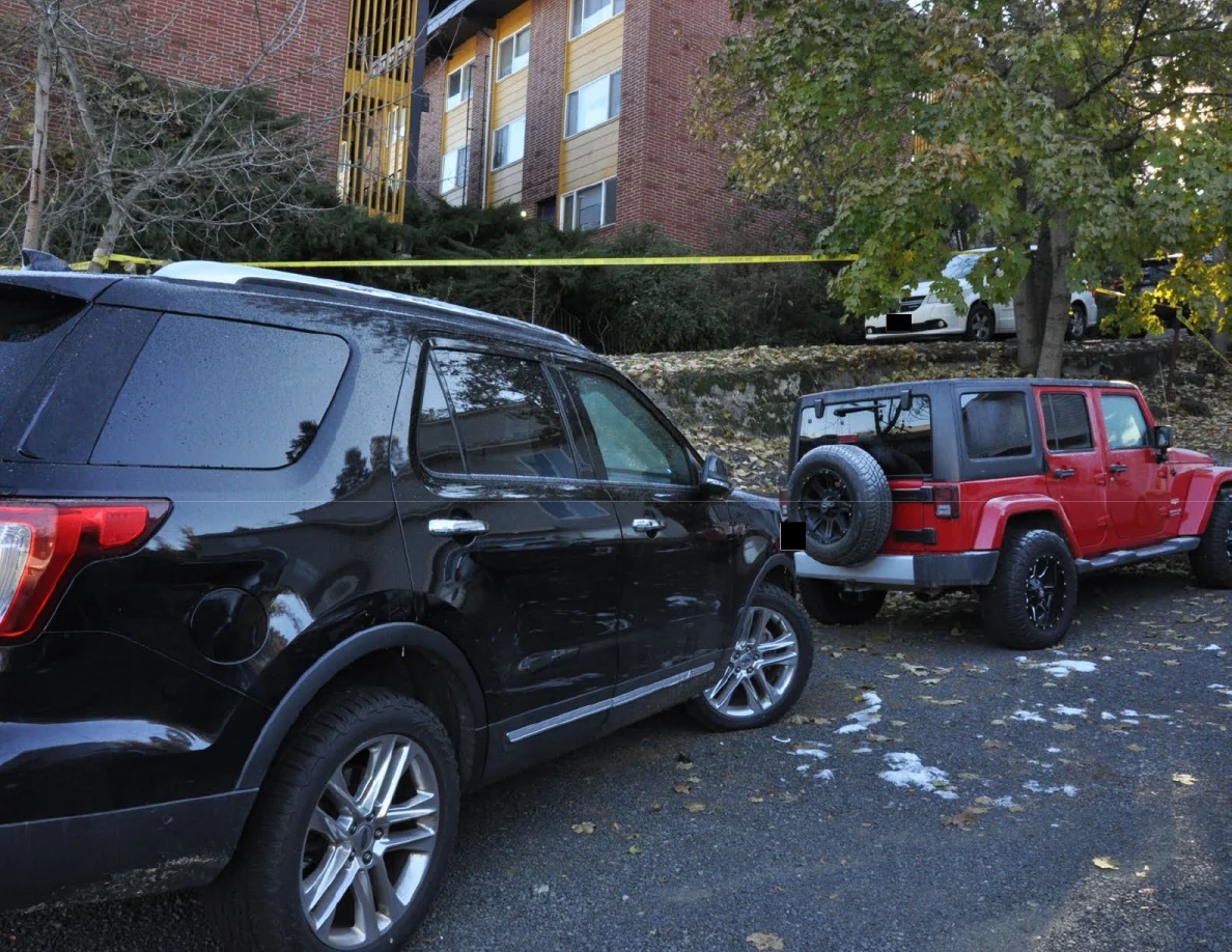 Black Ford SUV beside a red Jeep below a brick building and yellow tape.