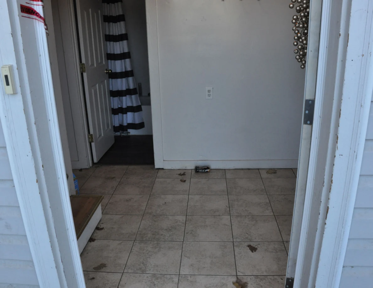 View through the entrance toward a tiled hallway and bathroom with a striped shower curtain.