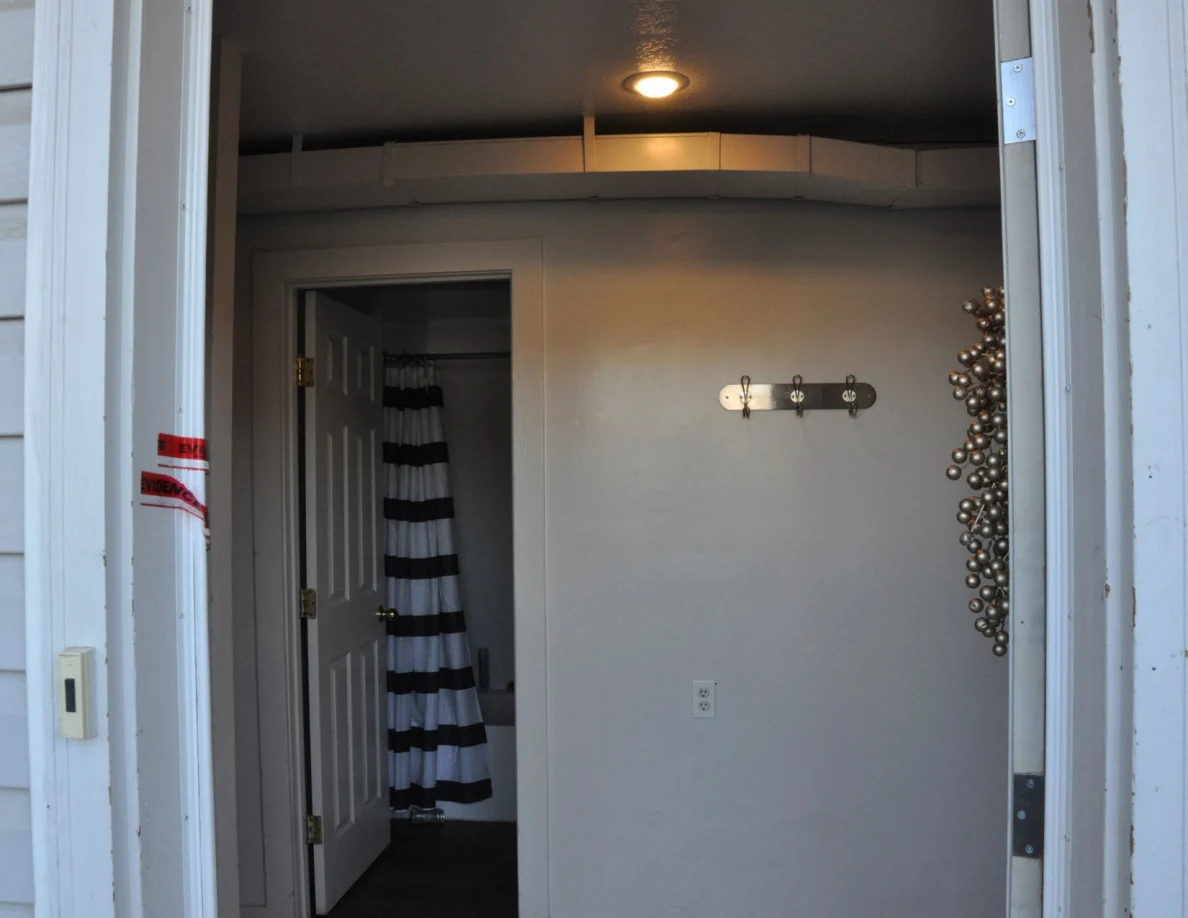 Entryway wall with coat hooks below exposed ductwork, beside a bathroom doorway.