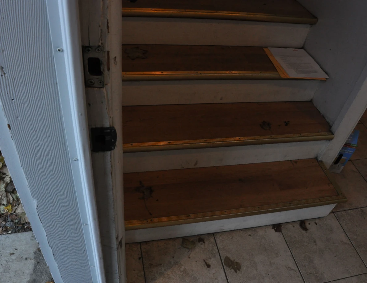 Lower wooden staircase with leaves and a paper lying on a step.