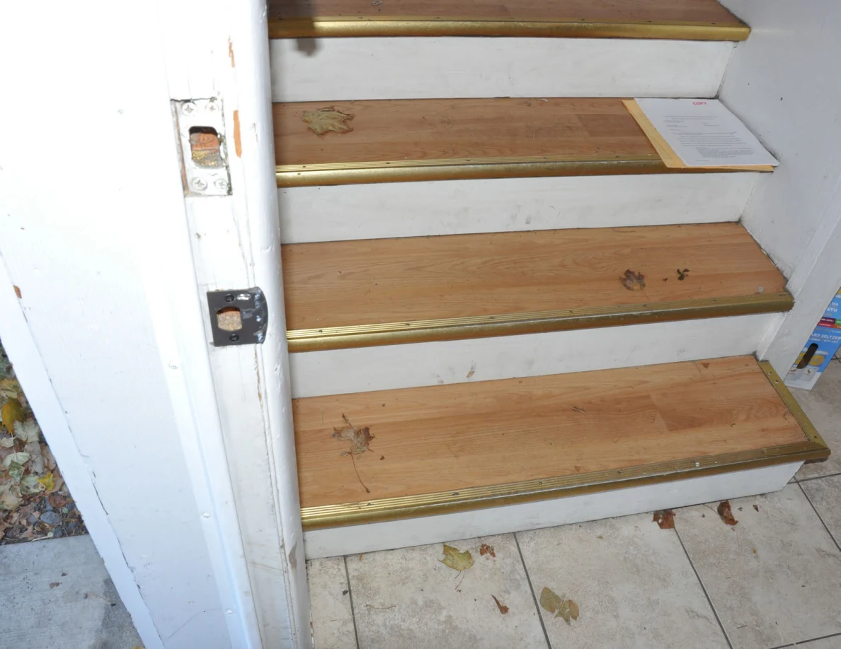 Wooden steps with gold-colored edges, scattered leaves and a paper on one tread.