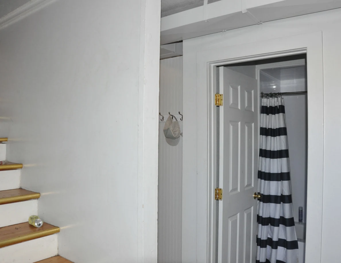 Staircase wall beside an open bathroom door and black-and-white striped shower curtain.