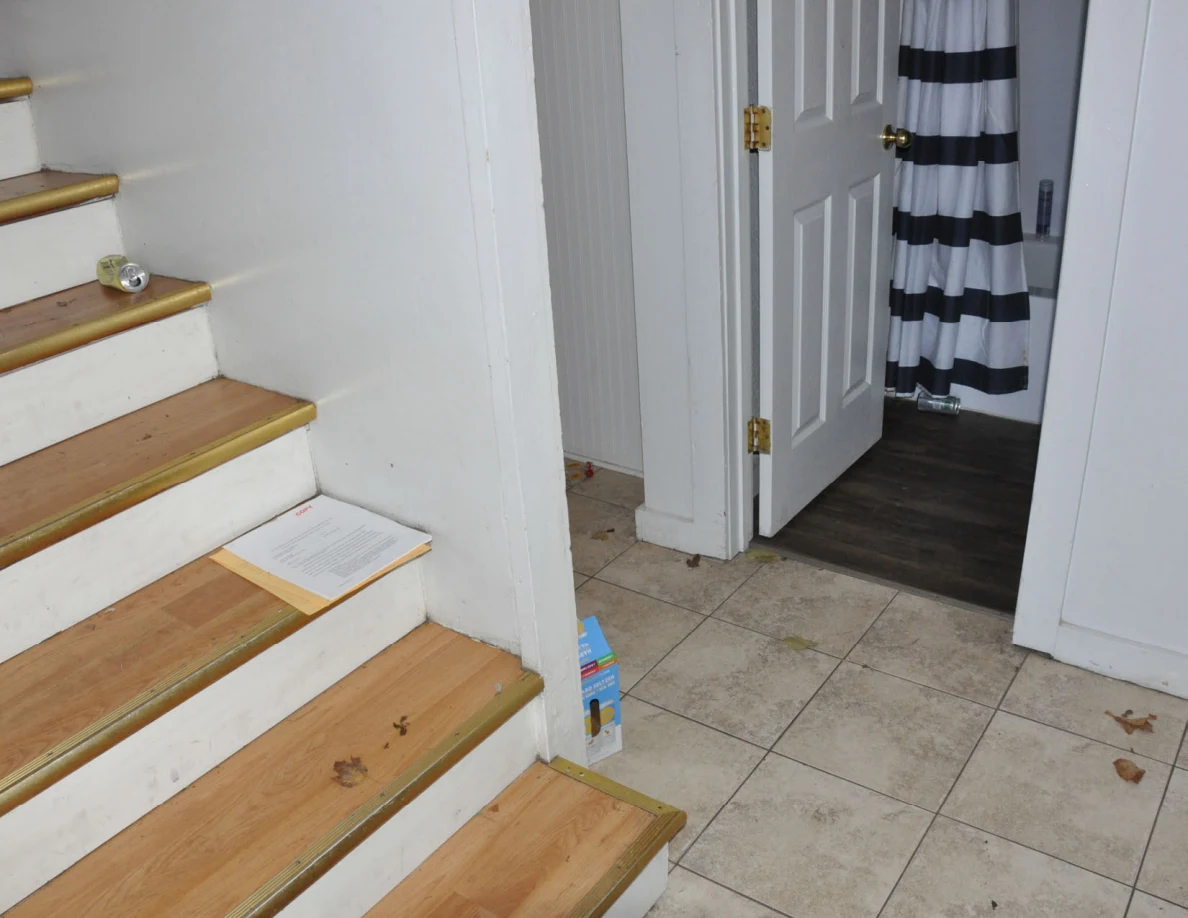Bottom of wooden staircase beside a tiled hallway and open bathroom door.