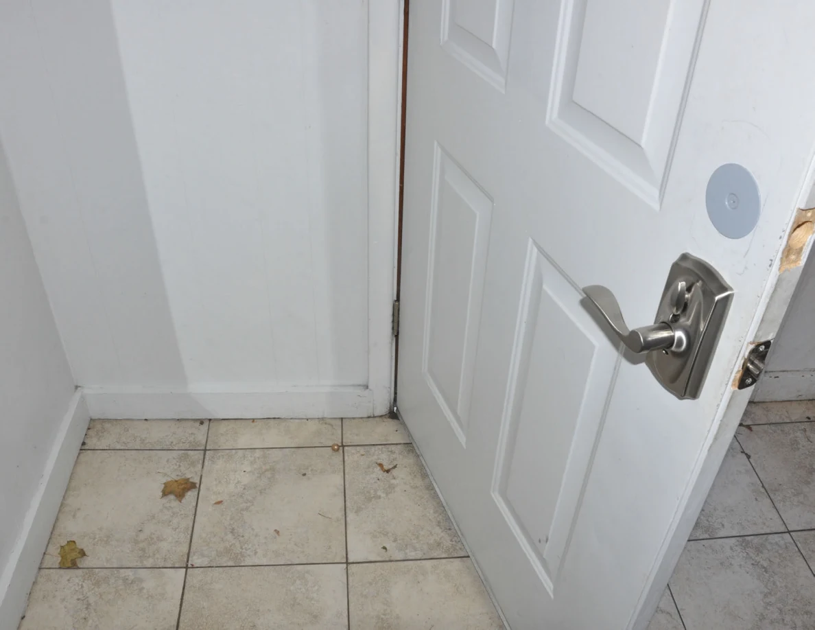 Interior side of a white entrance door with silver lever handle above a tiled floor.