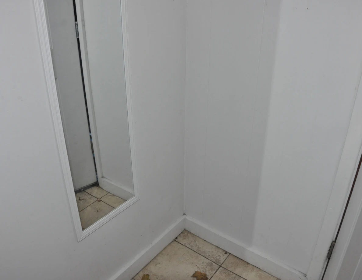 Narrow wall mirror and corner of a tiled entryway floor.