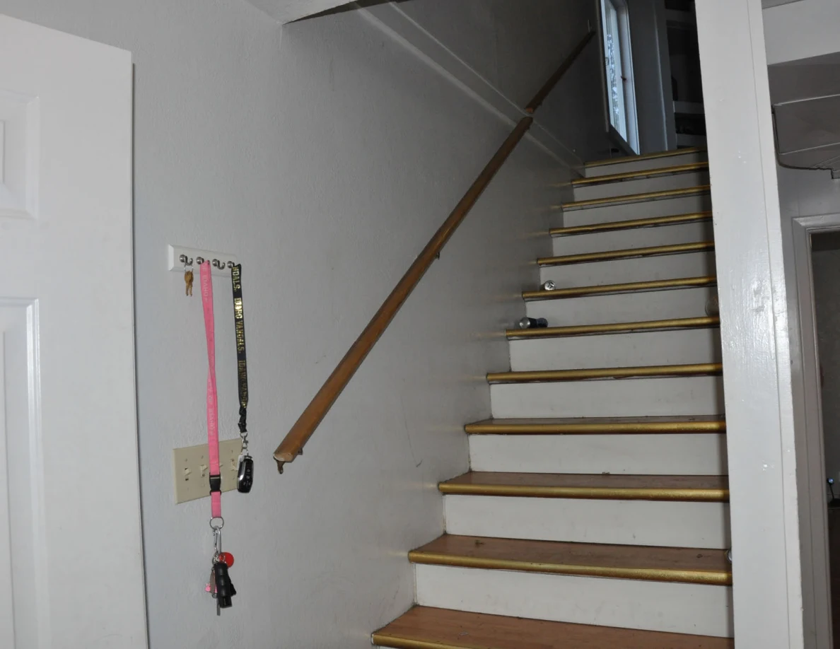 Wooden staircase with handrail, drink cans on steps and keys hanging from wall hooks.