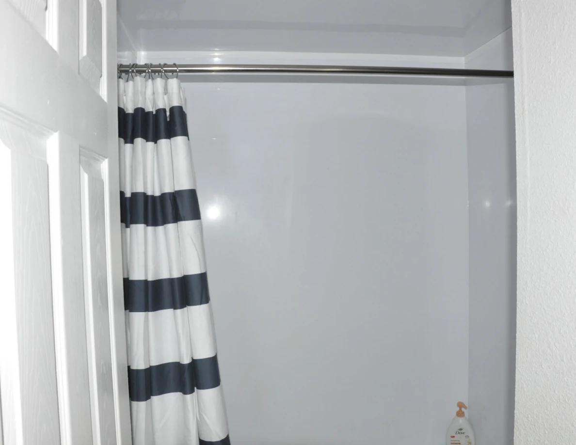 White bathtub surround with a black-and-white striped curtain and metal shower rod.